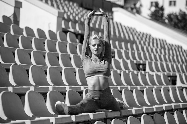 Femme sexy de remise en forme qui s'étend en tenue de sport s'asseoir en fente sur la fente du stade