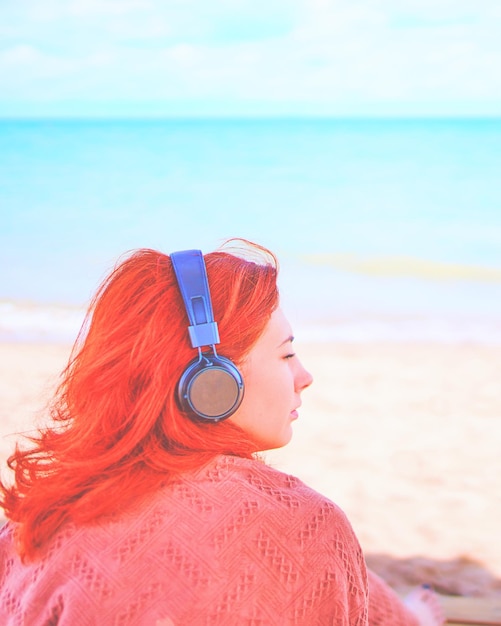 Femme sexy rousse écoutant de la musique sur la plage femme incroyable en pause bronzette sur la côte ...