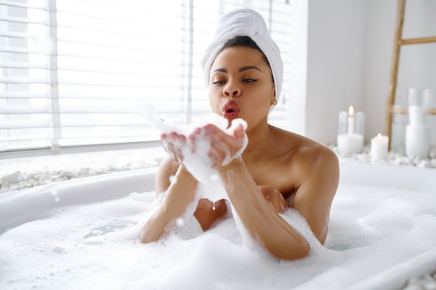 Femme sexy se détendre dans le bain avec de la mousse. Personne de sexe féminin dans la baignoire, soins de beauté et de santé au spa, traitement de bien-être dans la salle de bain, cailloux et bougies sur fond