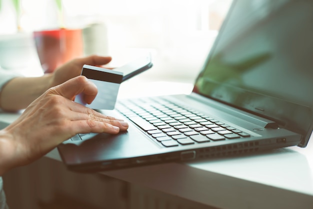 Femme shopping en ligne avec un smartphone. Mains de femme achète en ligne détenant une carte de crédit avec un ordinateur portable sur la table, assis dans un café.