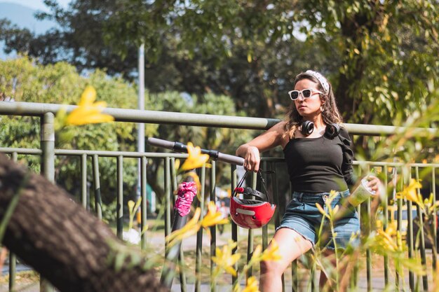 Femme en short avec une planche à roulettes électrique s'appuyant sur une clôture