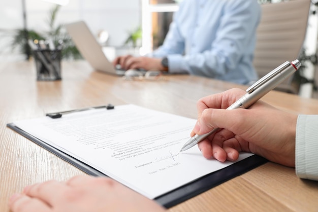 Femme signant un contrat à table en gros plan de bureau