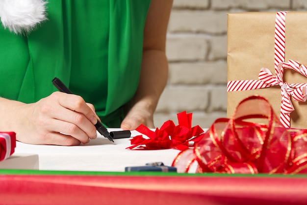 Femme signe des cadeaux de Noël avec un stylo noir. emballage de cadeaux de Noël