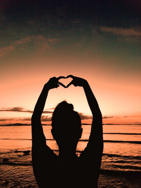 Photo une femme en silhouette debout sur la plage contre le ciel au coucher du soleil