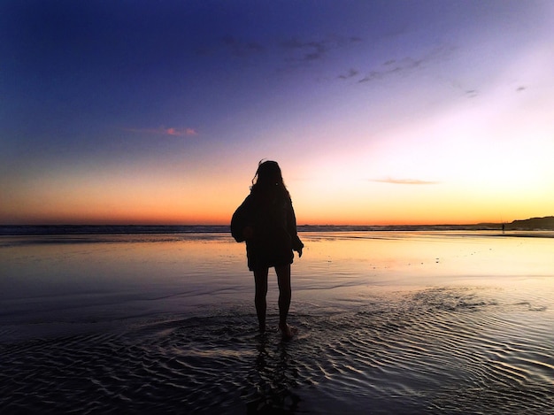 Une femme en silhouette debout sur la plage contre un ciel clair
