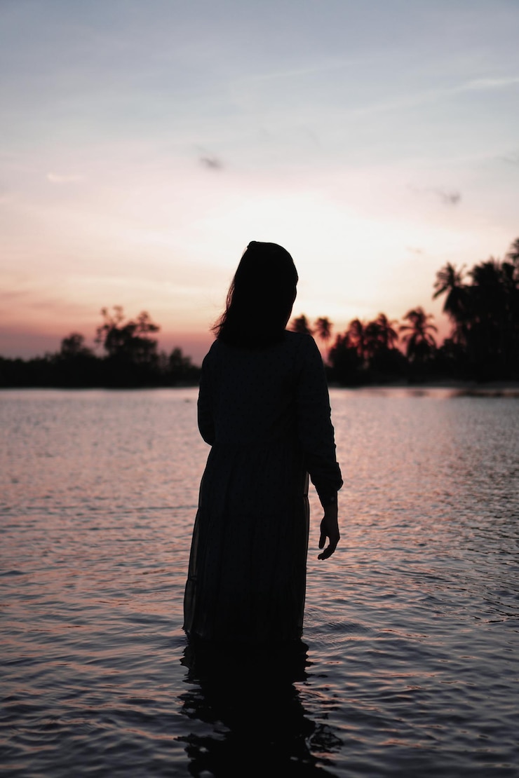 Photo femme en silhouette sur la plage au coucher du soleil
