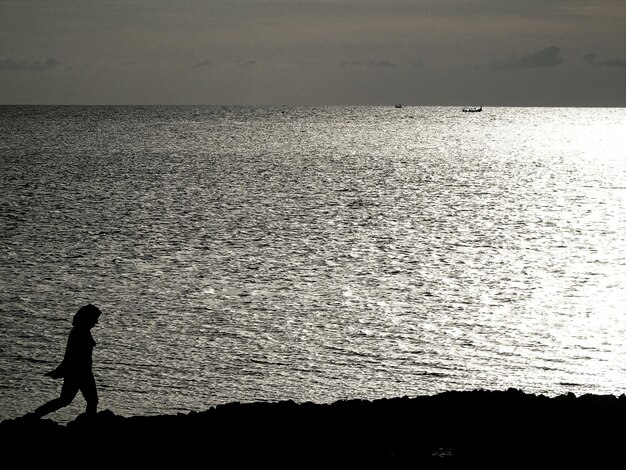 Photo une femme en silhouette se promène sur la plage contre le ciel au coucher du soleil