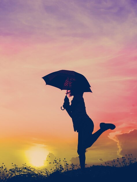 Photo une femme en silhouette tenant un parapluie contre le ciel orange