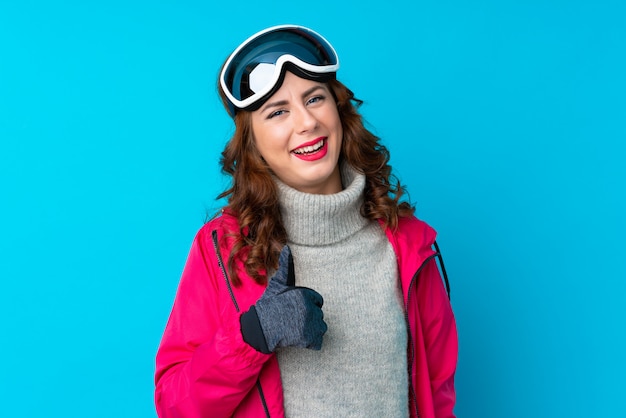 Femme de skieur avec des lunettes de snowboard sur mur bleu isolé, donnant un geste du pouce