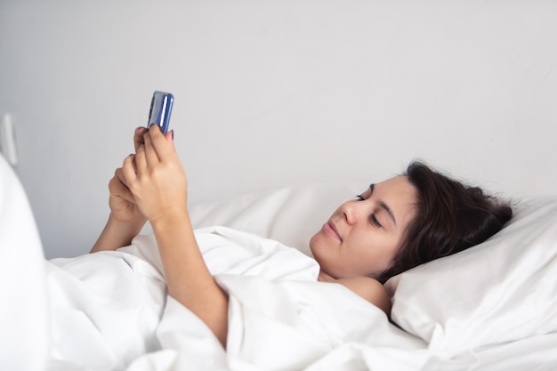 Femme avec smartphone au lit avec des draps blancs