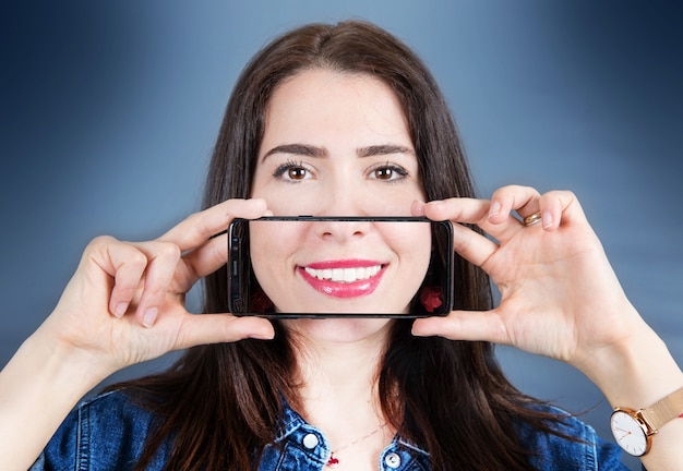 Femme avec smartphone qui prend une photo de son sourire