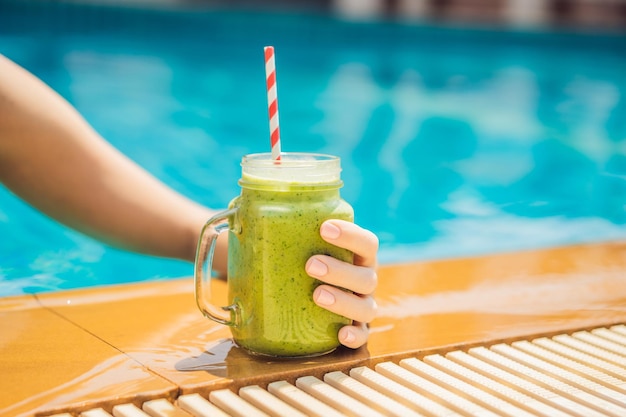 Femme avec un smoothie vert d'épinards et de banane sur le fond de la piscine Des aliments sains des smoothies sains