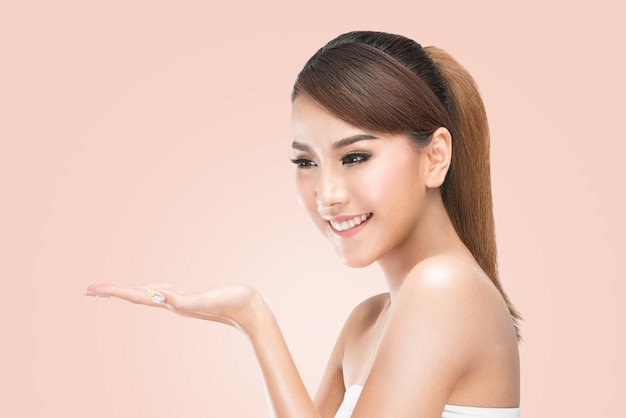 femme de soin de beauté femme asiatique montrant le produit sur le côté avec la main ouverte.