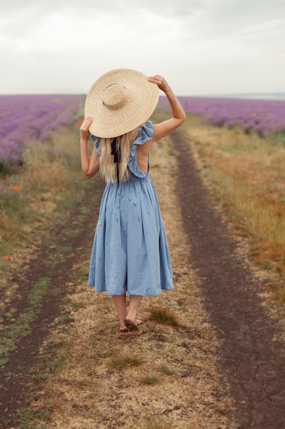 Femme sur un sol sale dans une robe bleue et un chapeau en osier entre des champs de lavande en Provence