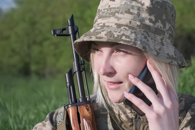 Une femme soldat ukrainienne avec un fusil d'assaut appelant quelqu'un au téléphone