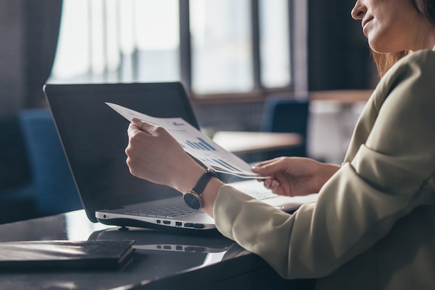 Femme à son bureau tient un document et regarde le graphique.