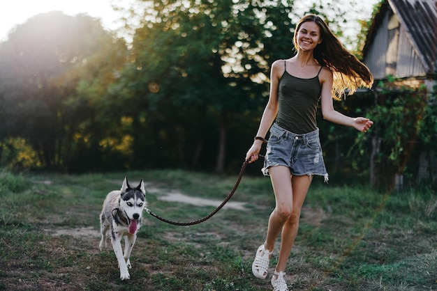 Femme et son chien husky courant joyeusement dans l'herbe dans la nature dans le parc sourire avec des dents tombent marcher avec un animal de compagnie voyageant avec un ami chien