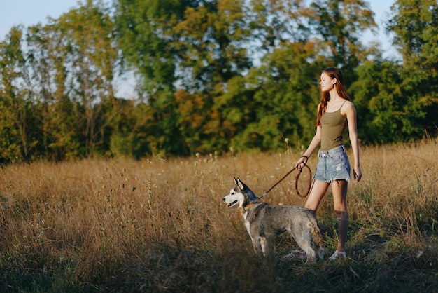 Une femme et son chien husky marchent et courent joyeusement dans l'herbe sur le terrain sourire avec des dents automne coucher de soleil marcher avec un animal de compagnie voyager avec un ami chien bonheur style de vie