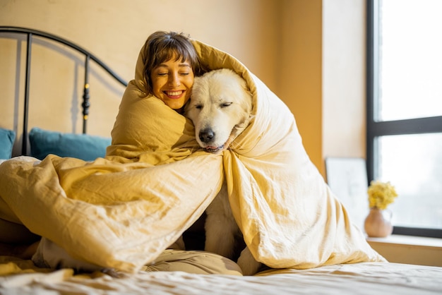 Femme avec son chien sous la couverture sur le lit