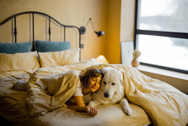 Femme avec son chien sous la couverture sur le lit