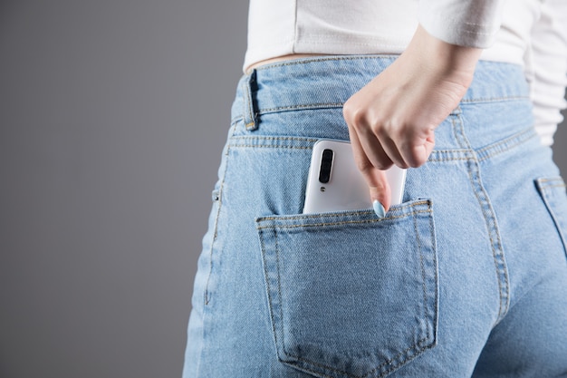 Femme sort un téléphone de sa poche sur un mur gris