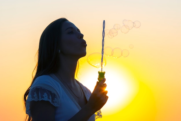 Une femme souffle des bulles sur fond de soleil couchant. plaisirs d'été et loisirs de plein air