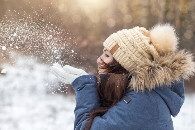 Photo une femme souffle de la neige de ses paumes sur fond de paysage hivernal