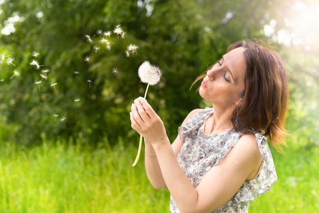 Une femme souffle un pissenlit dans la nature. Heureuse femme marchant dans le parc.