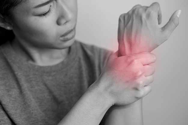 Femme souffrant de douleurs au poignet. Douleur au poignet d'une femme. Jeune femme tenant son poignet douloureux sur fond de mur.