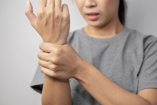 Femme souffrant de douleurs au poignet. Douleur au poignet d'une femme. Jeune femme tenant son poignet douloureux sur fond de mur.