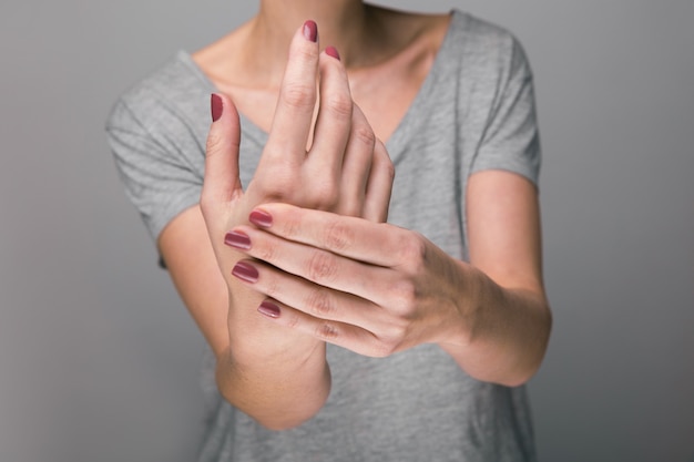 Femme souffrant de douleurs osseuses sur fond gris, Concept avec grimace d'arthrite à la main dans la douleur