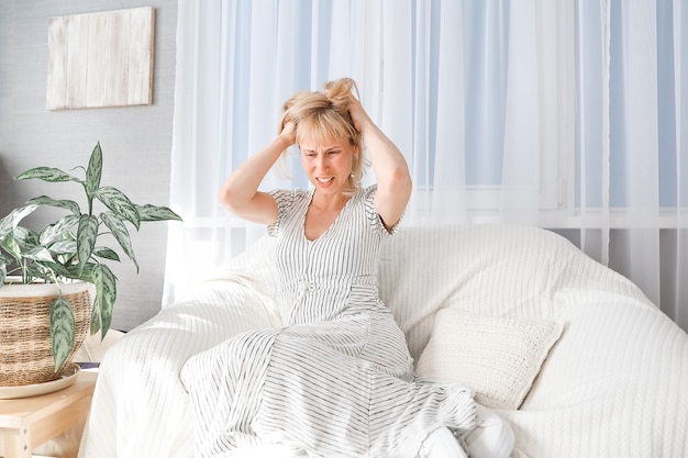 Une femme souffrant de maux de tête est assise sur une chaise dans le salon. Thérapie psychologique, pas d'énergie, manque de sommeil