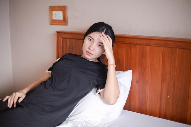 Femme souffrant de maux de tête Photo en gros plan d'une belle femme assise sur un lit dans sa chambre, les yeux fermés, touchant sa tête alors qu'elle souffre d'une migraine