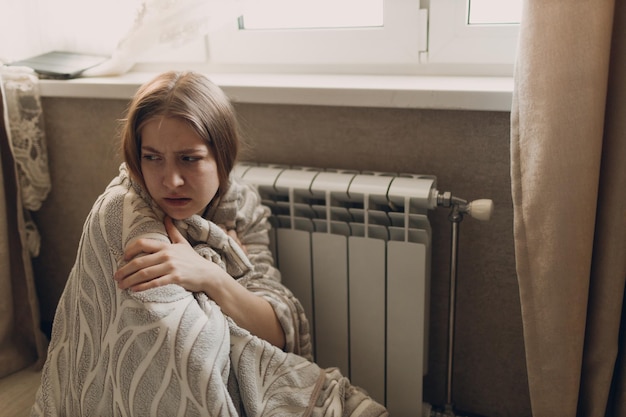 Une femme souffrante dans un plaid est assise devant la batterie de chauffage de la maison et se fige