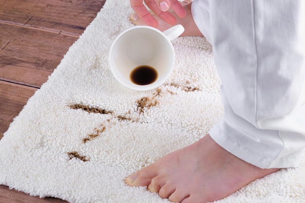 Une femme soulevant une tasse de café renversé sur un tapis. Échec domestique. concept de tache de la vie quotidienne