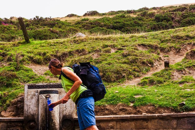 Une femme à la source d'eau remplissant sa bouteille d'eau pendant le Camino de Santiago