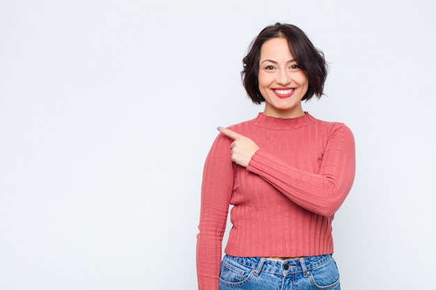 Femme souriant joyeusement, se sentant heureux et pointant vers le côté et vers le haut, montrant l'objet dans l'espace de copie