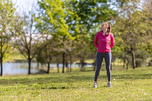 Une femme souriante adulte en vêtements de sport debout sur le terrain et regardant sur le côté