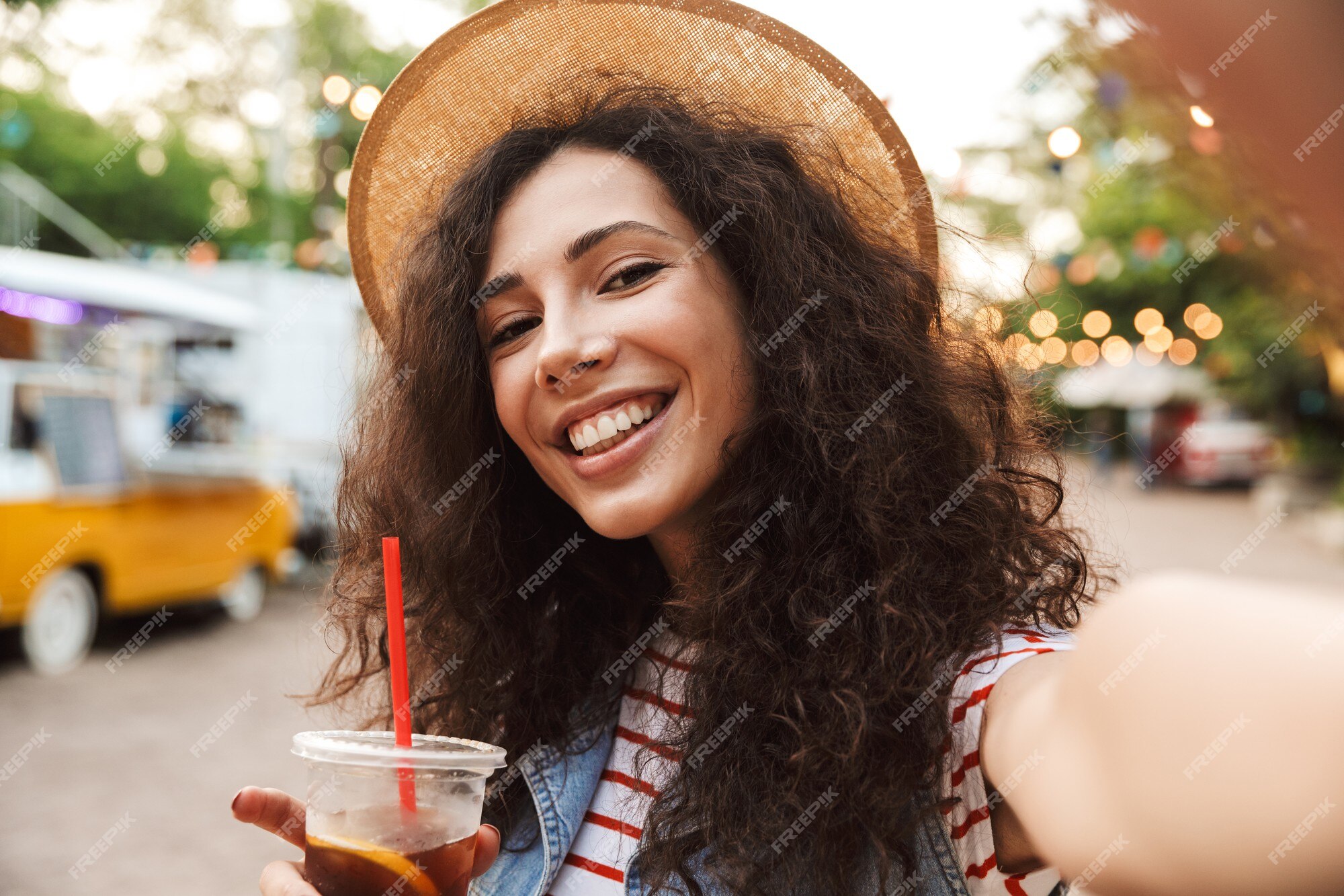 Femme Souriante Affable Aux Cheveux Bruns Bouclés Portant Un Chapeau De  Paille D'été Souriant Et Buvant Du Thé Froid Dans Une Tasse En Plastique En  Plein Air, Tout En Prenant Une Photo De Selfie