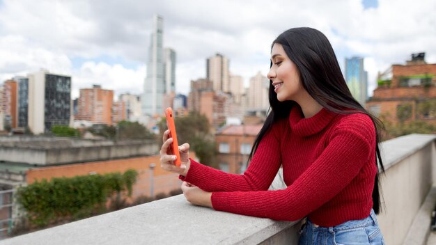 Femme souriante à l'aide d'un smartphone Fille aux cheveux noirs et à la veste rouge sourit à l'aide d'un smartphone