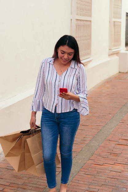 Femme souriante à l'aide d'un téléphone intelligent en se tenant debout dans la ville