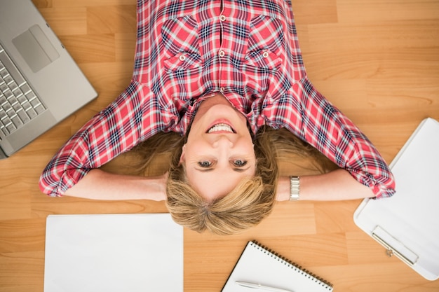 Femme souriante allongé sur le sol entouré d&#39;articles de bureau