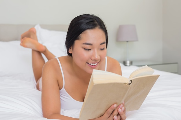 Femme souriante allongée sur le lit en lisant