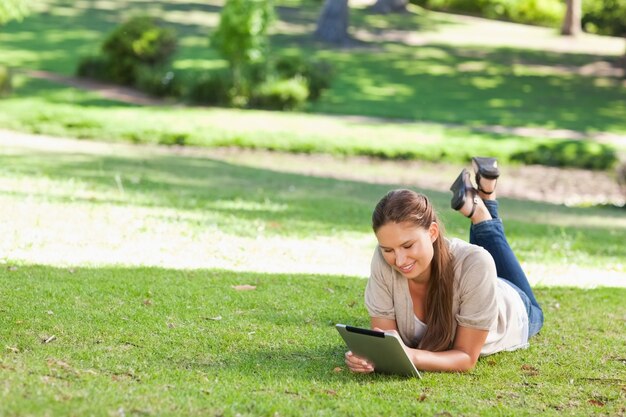 Femme souriante allongée sur la pelouse avec une tablette