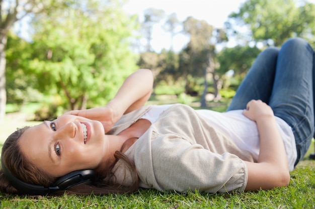 Femme souriante allongée sur la pelouse tout en écoutant de la musique