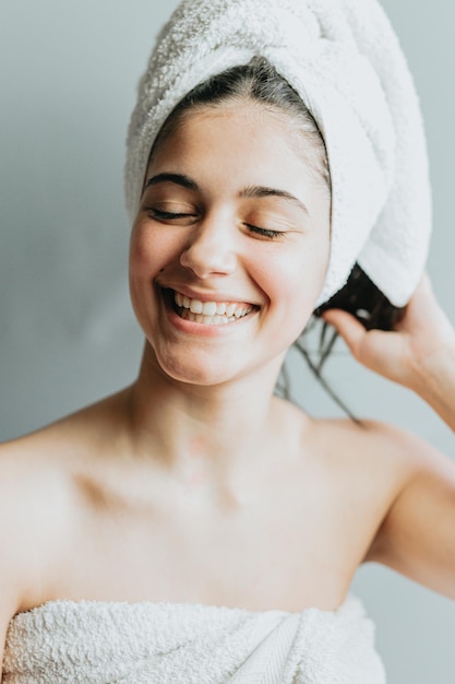 Une femme souriante assez calme avec une serviette enveloppante sur la tête profite de la douceur d'une peau éclatante et d'un traitement capillaire Gel de soin ou hydratant Détendu après le bain isolé sur fond gris