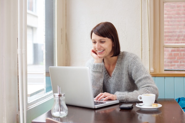 Femme souriante assise au café avec ordinateur portable