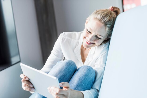 Femme souriante assise sur un canapé à l'aide d'une tablette