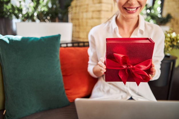 Femme souriante assise sur le canapé avec un cadeau en mains