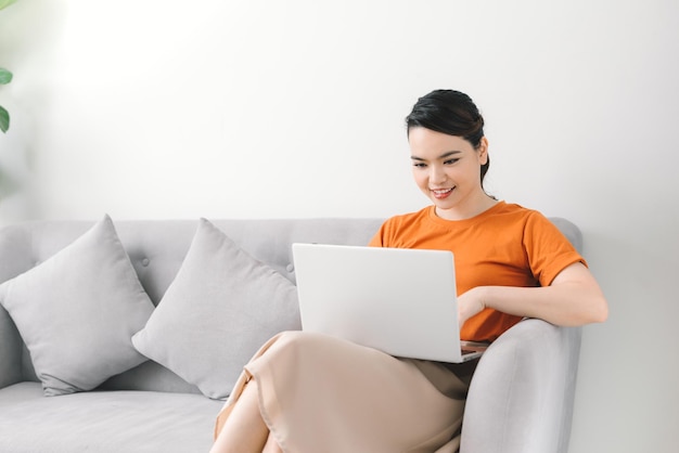 Femme souriante assise sur un canapé se détendre tout en naviguant sur le site Web d'achat en ligne